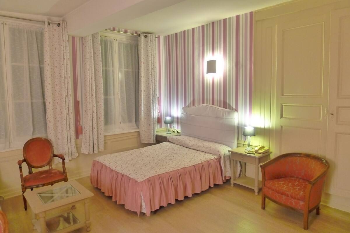 A bedroom with a bed, two chairs, a nightstand, and a lamp.