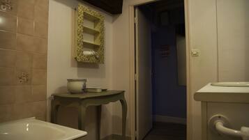 A bathroom with a bathtub, a sink, and a toilet. There is a mirror with a floral frame above the sink.