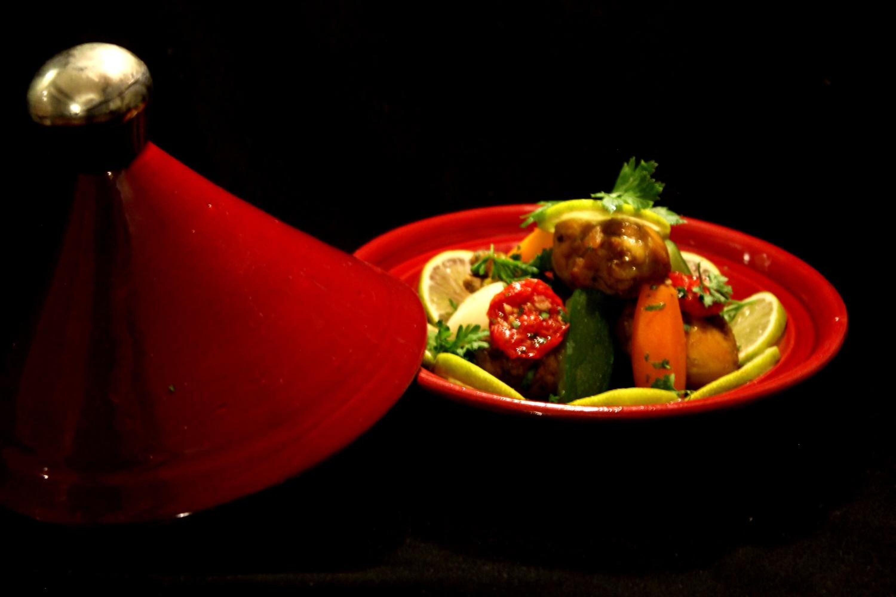 A red plate with a variety of vegetables and a lemon wedge.
