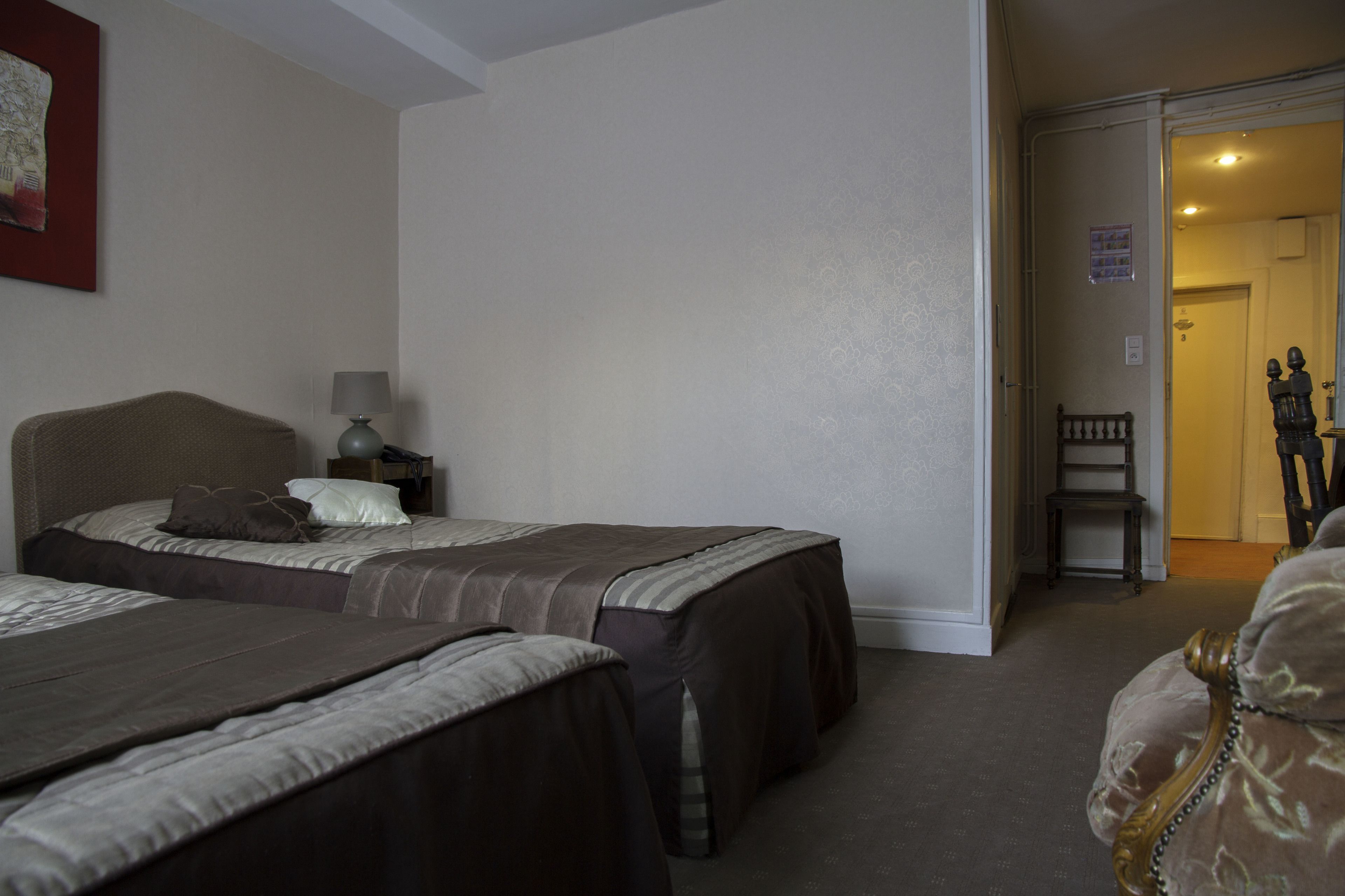 A hotel room with two beds, a nightstand with a lamp, and a chair in the corner.