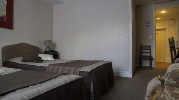 A hotel room with two beds, a nightstand with a lamp, and a chair in the corner.
