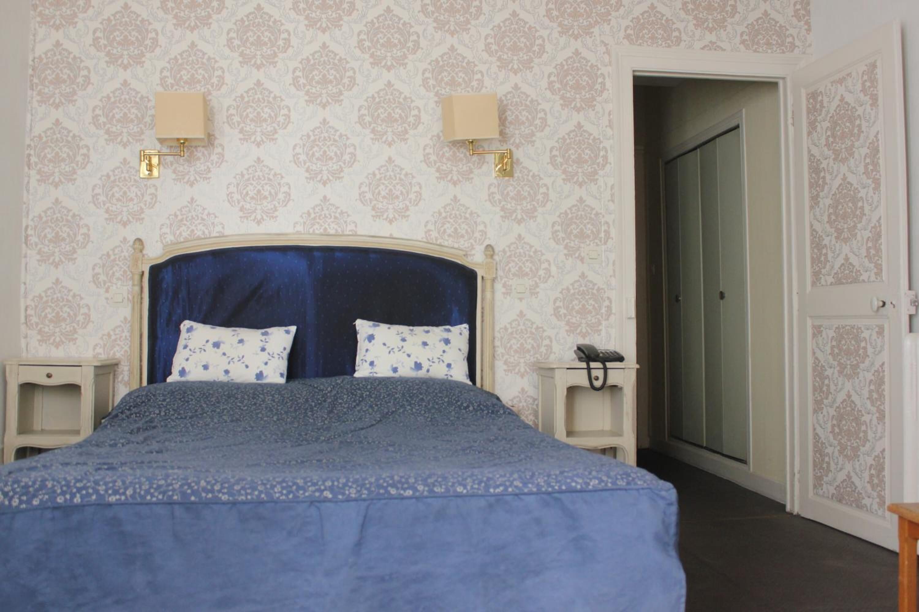 A bedroom with a bed, two bedside tables, a nightstand, a wall-mounted lamp, and a door leading to another room.
