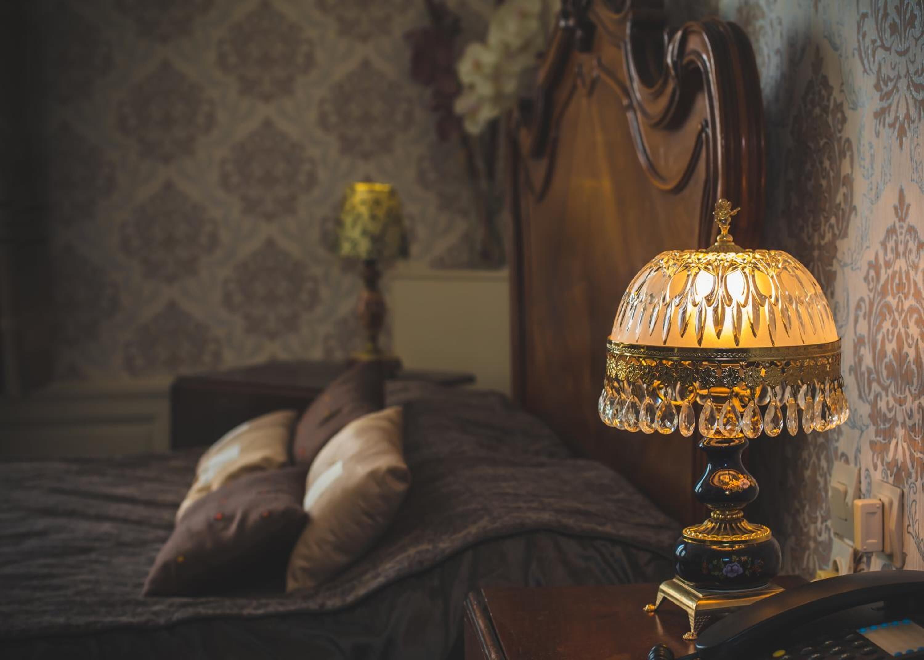 A bedroom with a bed, a nightstand, a lamp, and a telephone.