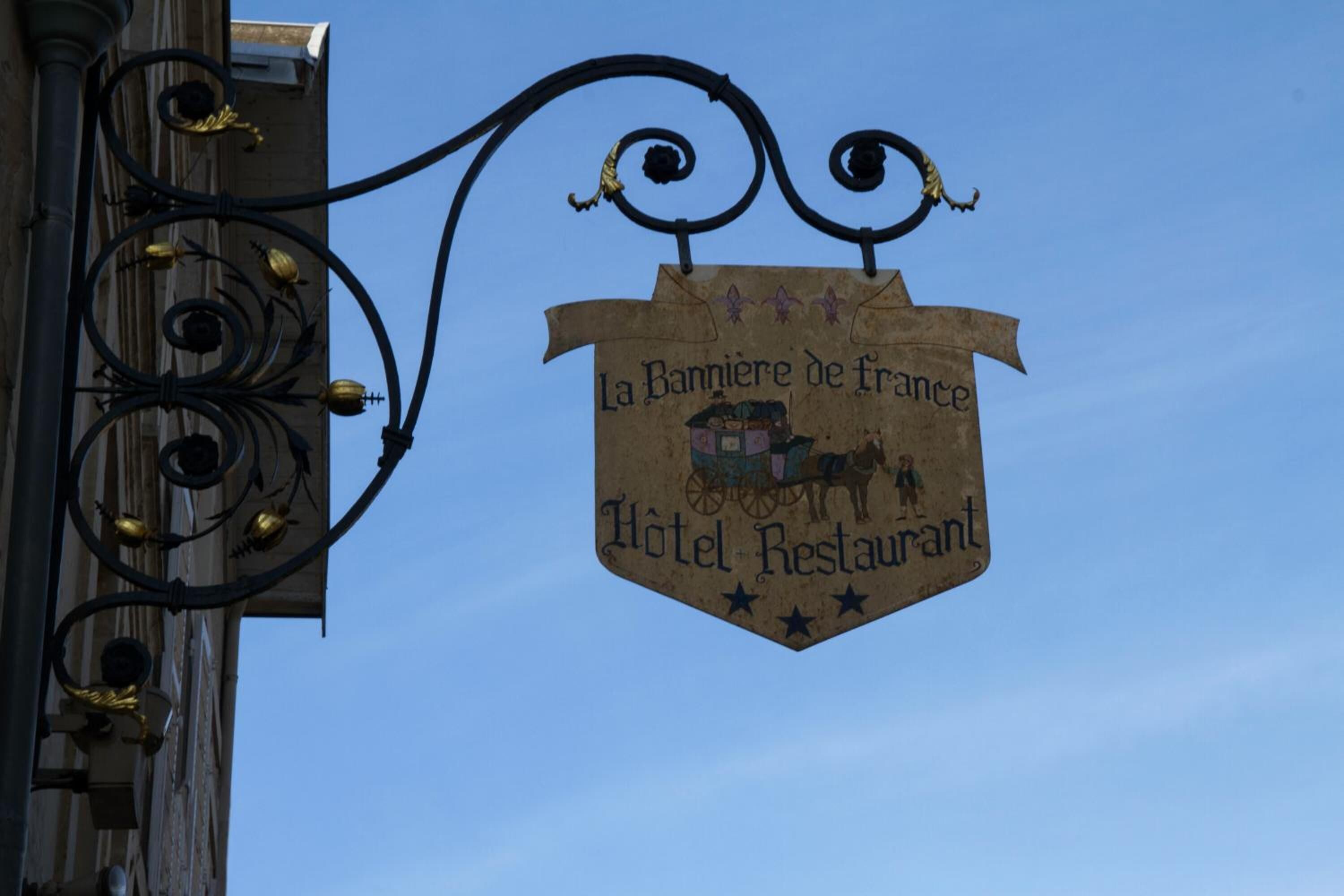 A sign for "La Banniere de France Hotel Restaurant" with a horse-drawn carriage illustration.