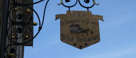 A sign for "La Banniere de France Hotel Restaurant" with a horse-drawn carriage illustration.