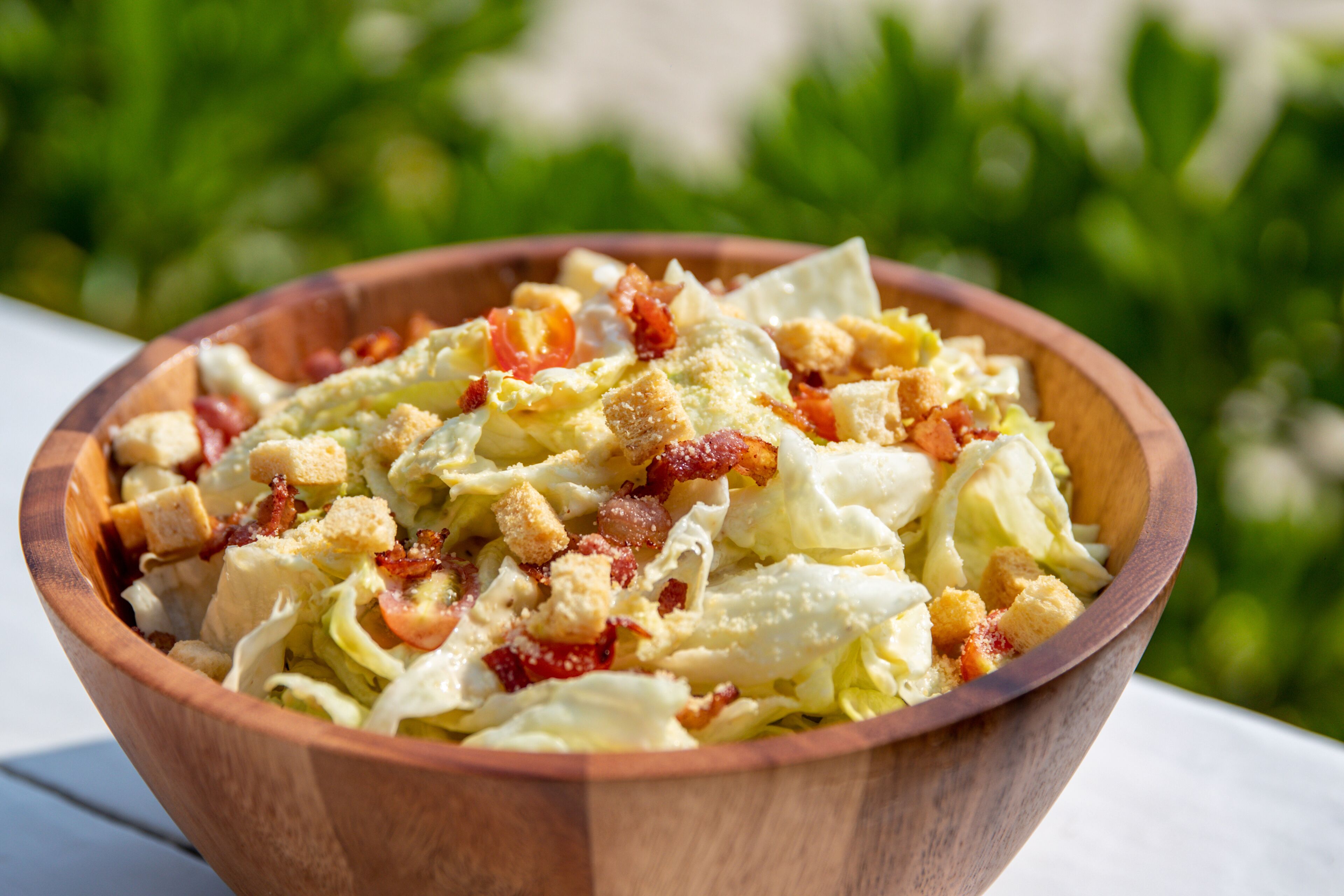 A wooden bowl of salad with croutons and bacon bits.