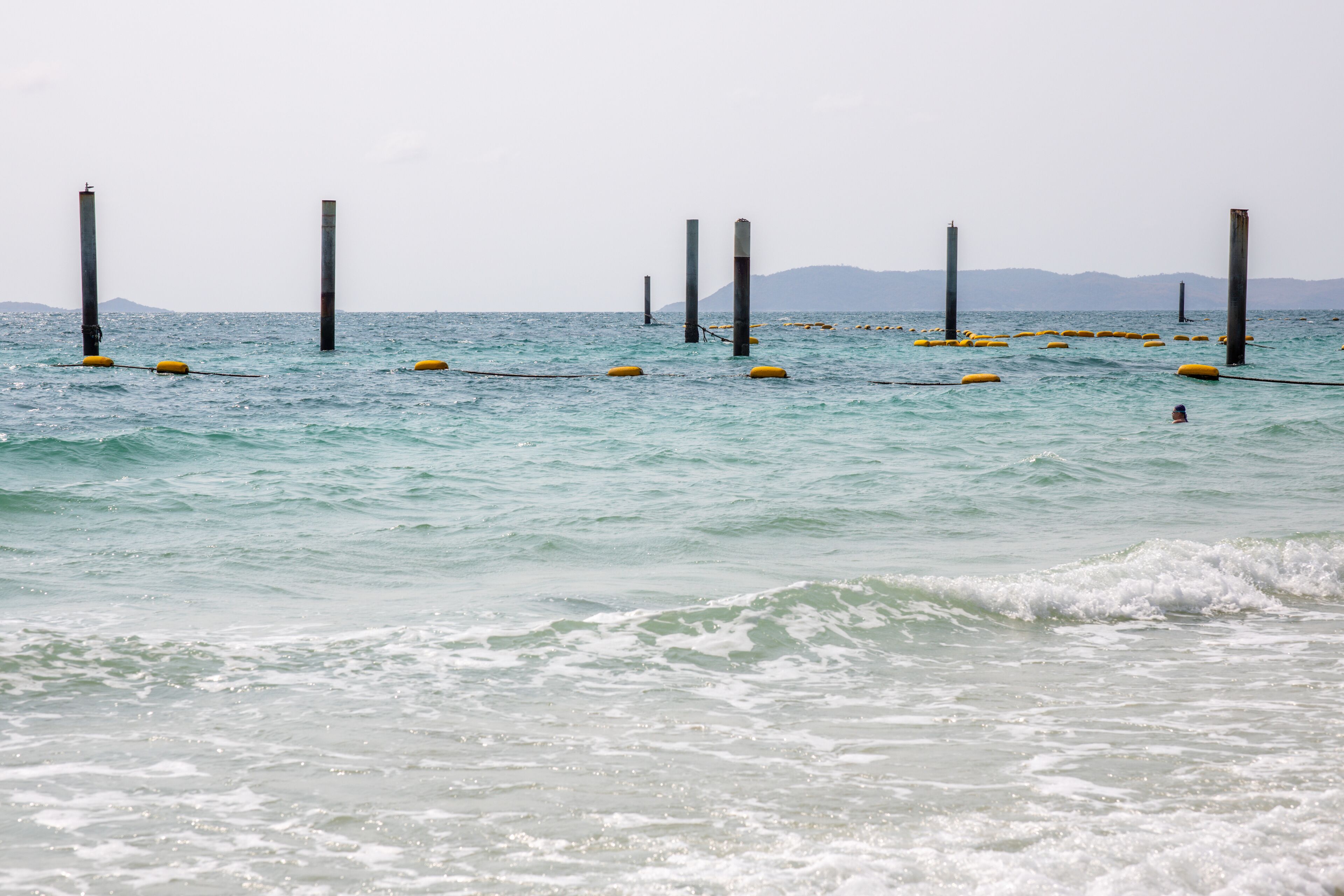 Escena costera con aguas tranquilas, boyas amarillas y postes altos.