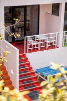 Una escalera conduce a un balcón con una mesa y sillas blancas, una mesa azul y un suelo con baldosas rojas y negras.