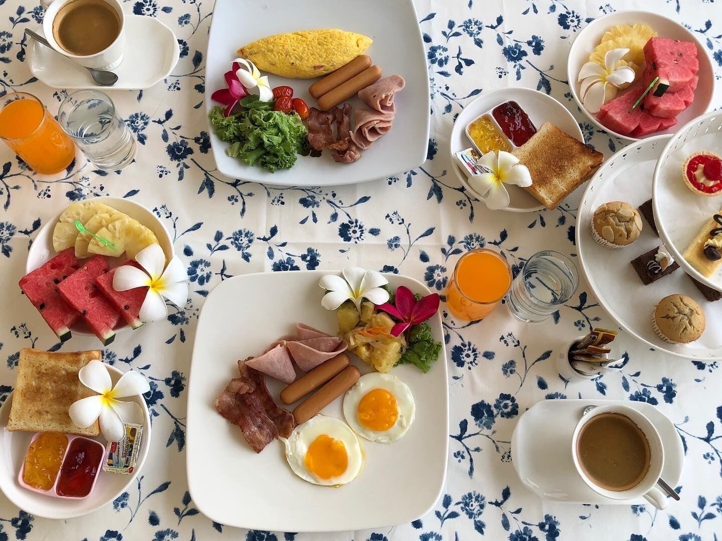 En frukostbuffé med olika rätter, drycker och ett blommigttryckt bordsduk.