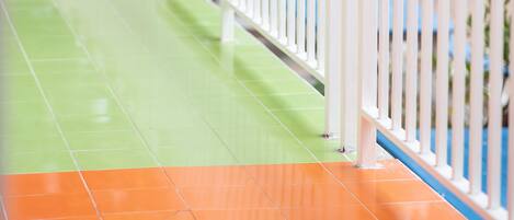 A corridor with a white railing, green and orange tiled floor, and trees in the background.