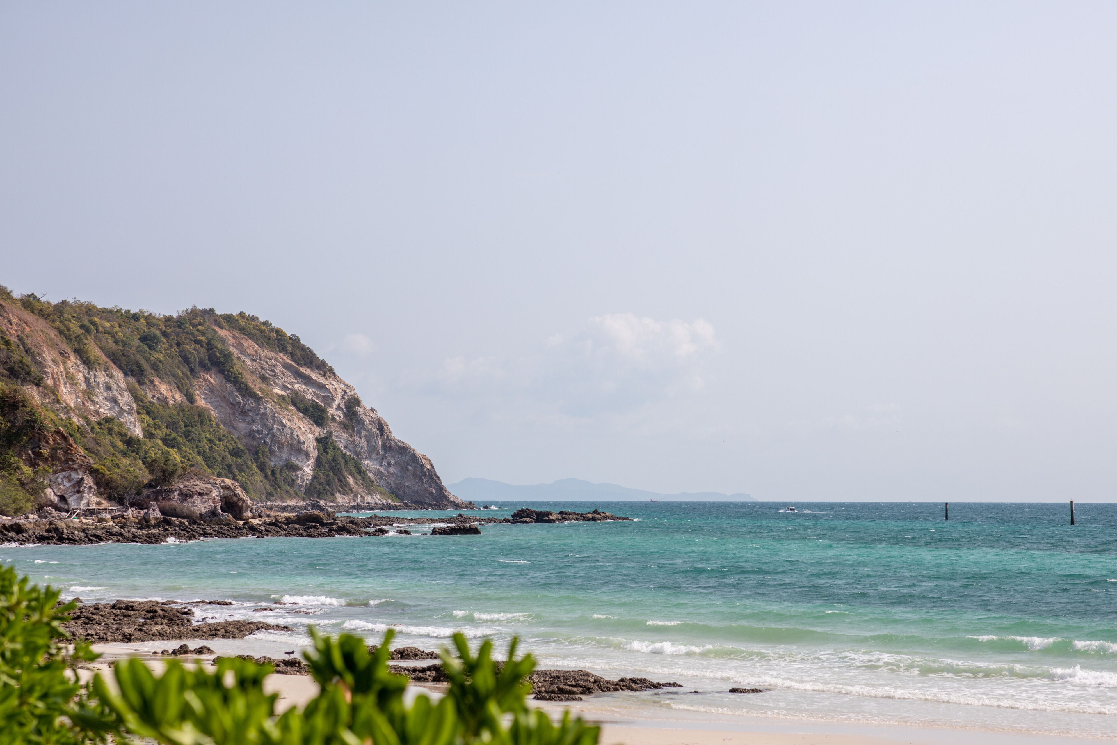 Un paysage côtier avec une falaise rocheuse, une mer calme et une plage de sable.