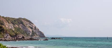 Un paysage côtier avec une falaise rocheuse, une mer calme et une plage de sable.