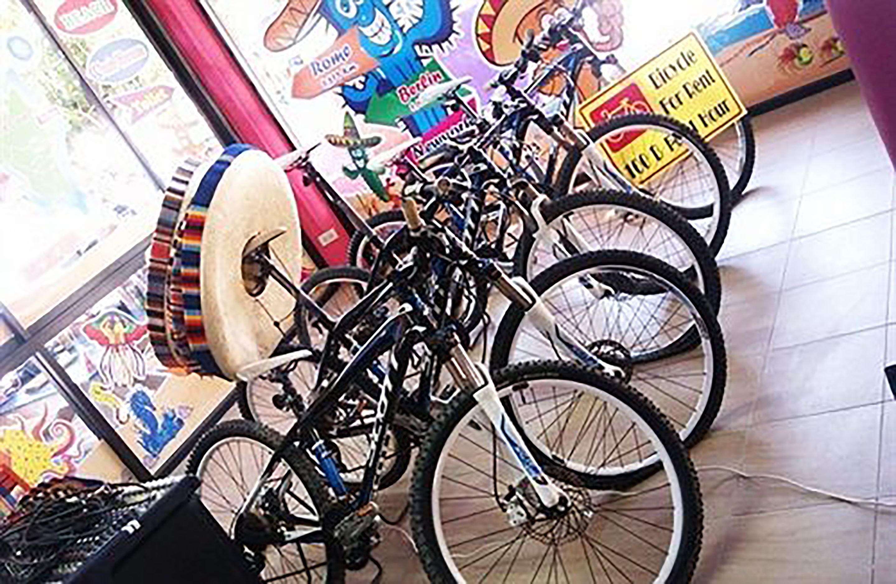 Una habitación con bicicletas aparcadas contra la pared, un cartel grande con un personaje de caricatura y un letrero que indica un servicio de alquiler de bicicletas.