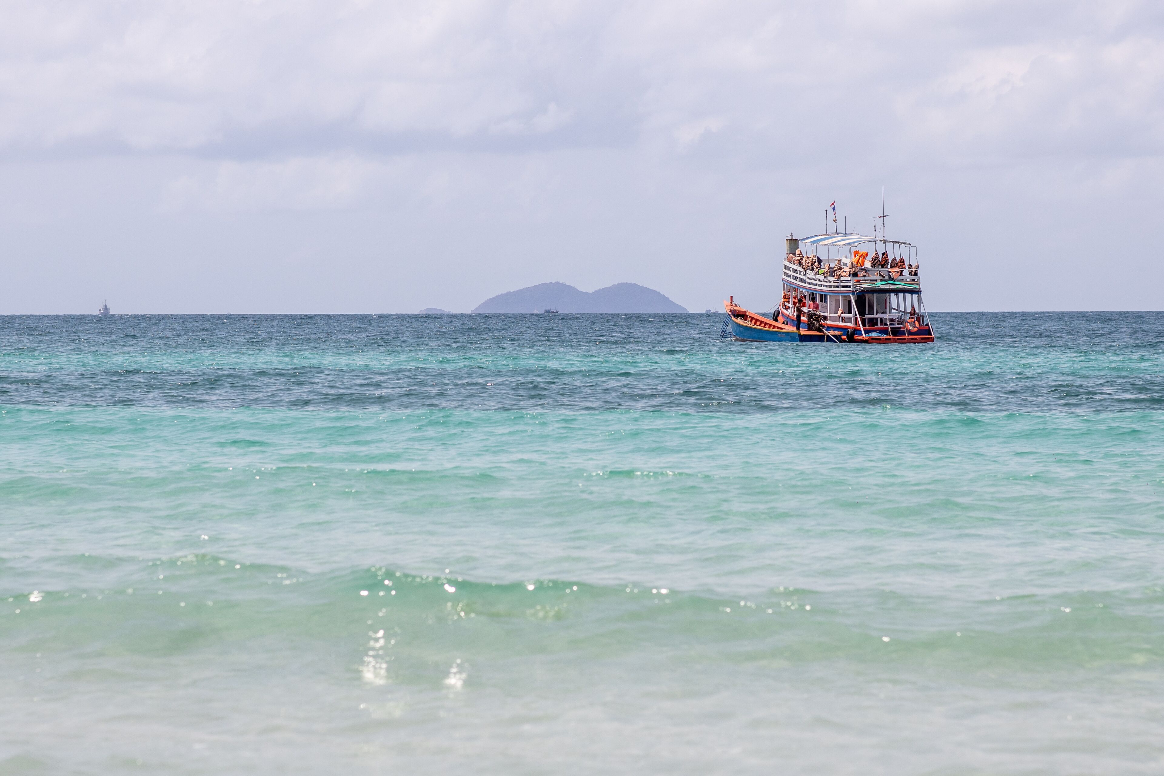 A boat with passengers on a calm sea, a distant island, and a cloudy sky.