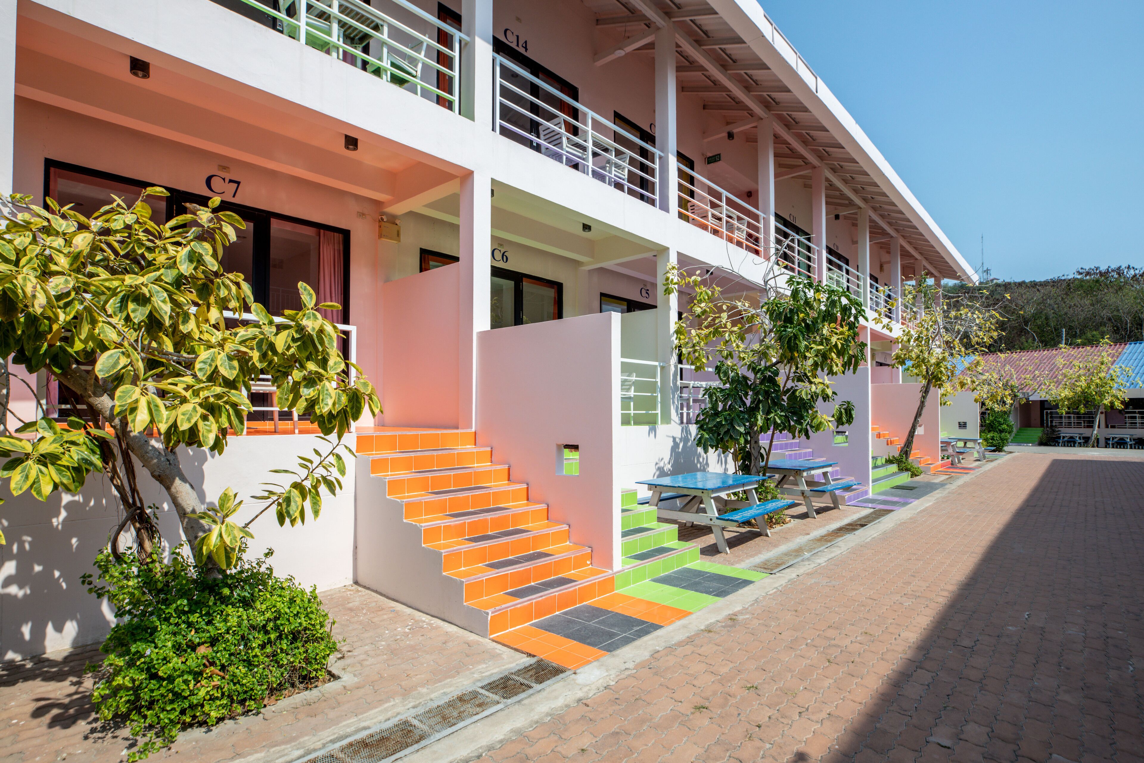 A multi-story building with a staircase leading to the entrance, outdoor seating, and greenery.