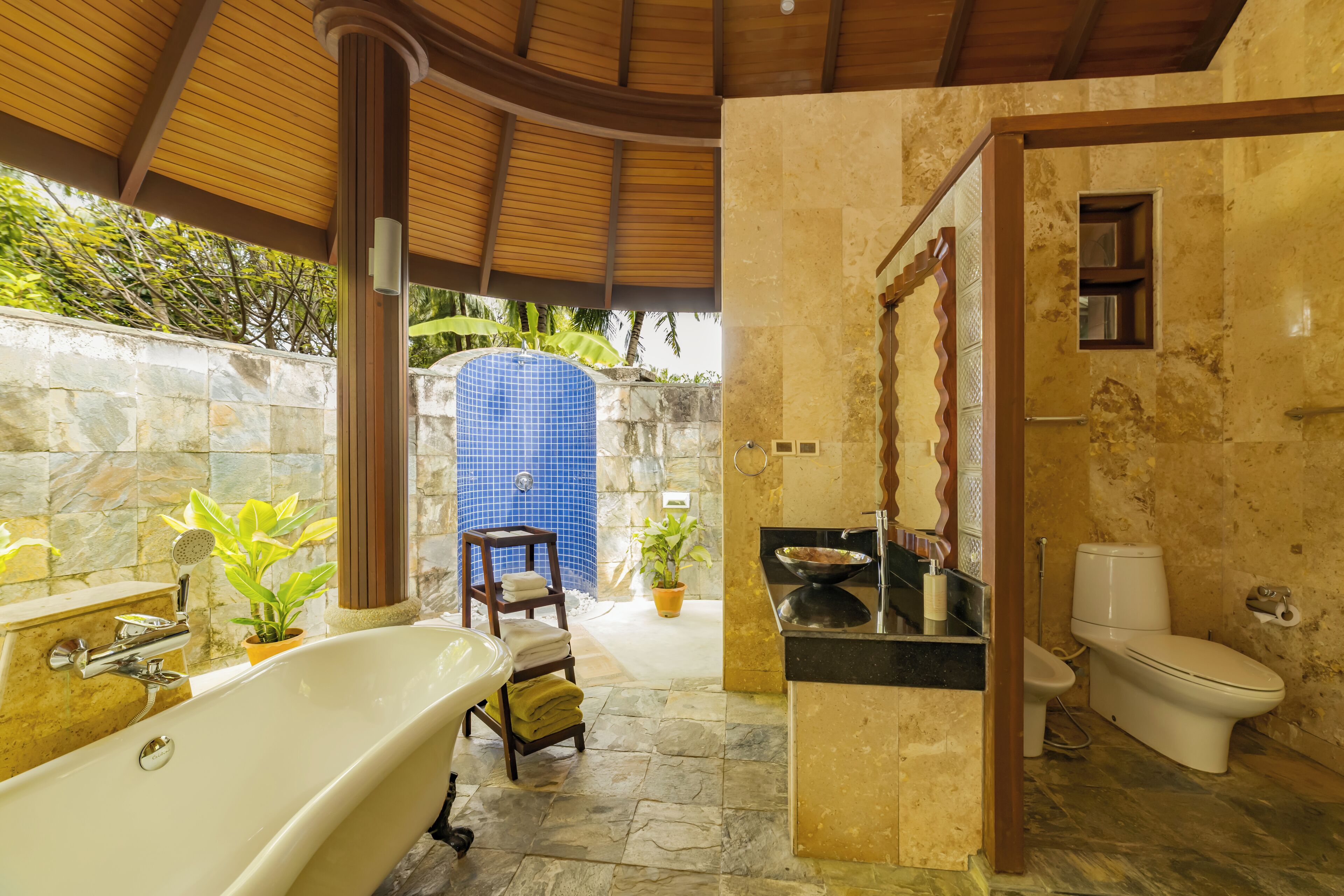 A bathroom with a bathtub, toilet, and sink. There are plants and a wooden chair.