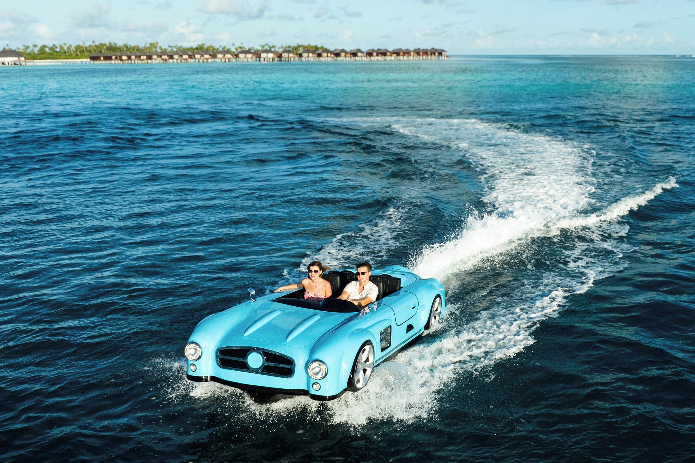 A blue convertible car driving on water with a person in the back seat.