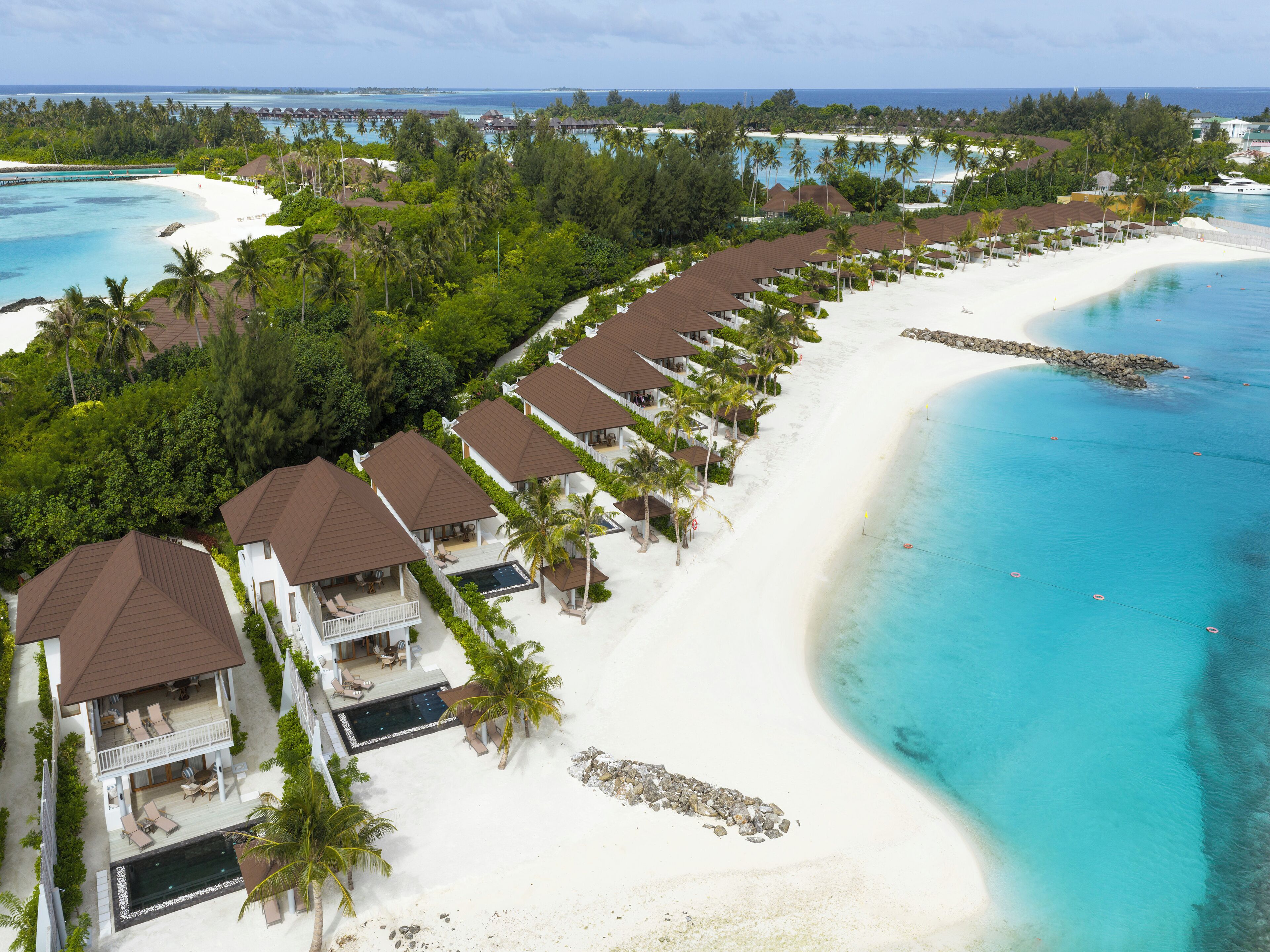 A resort with multiple bungalow-style buildings, a white sandy beach, and a clear turquoise ocean.