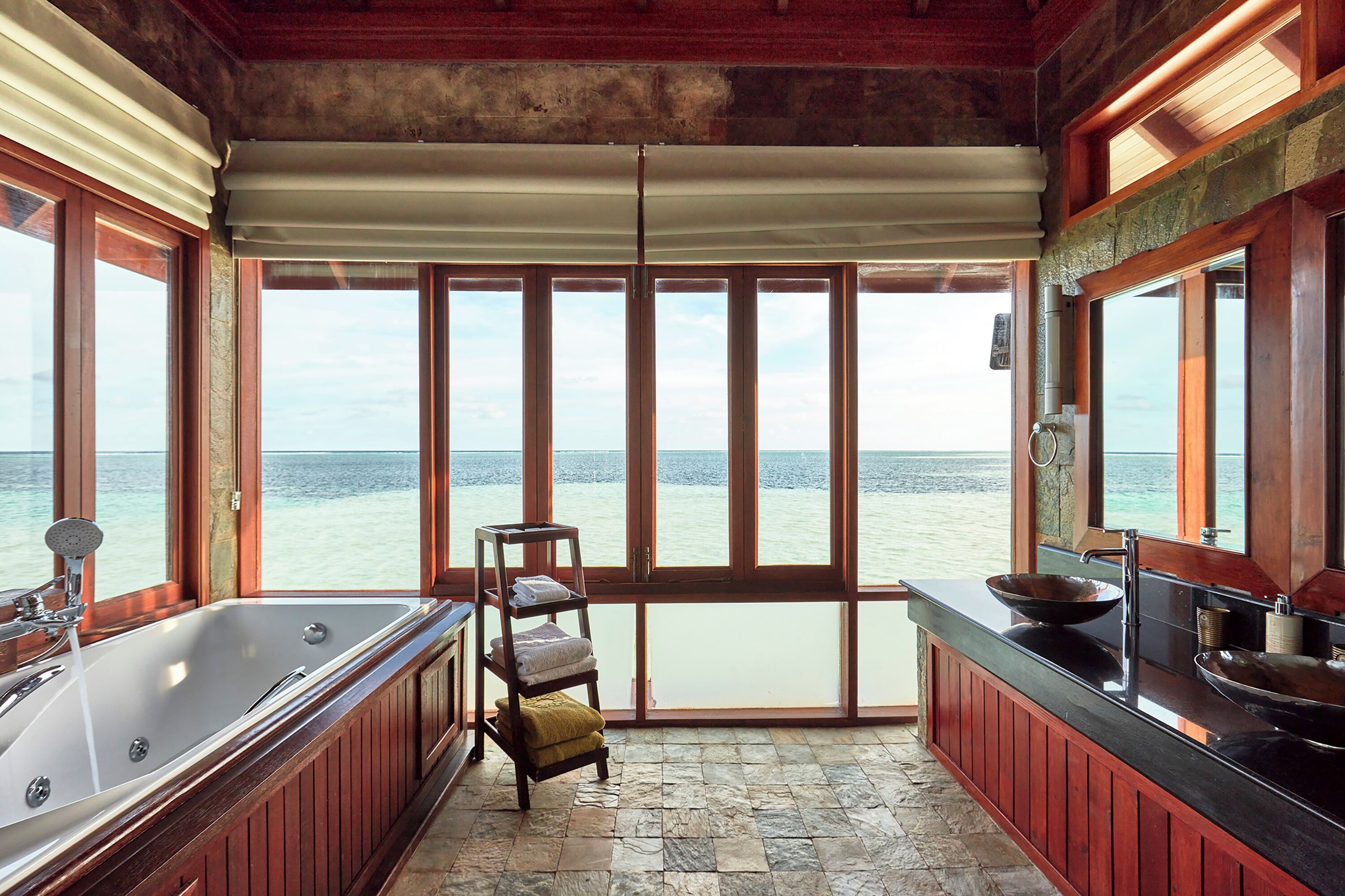A bathroom with a large bathtub, a sink, and a towel rack. There is a view of the ocean through large windows.