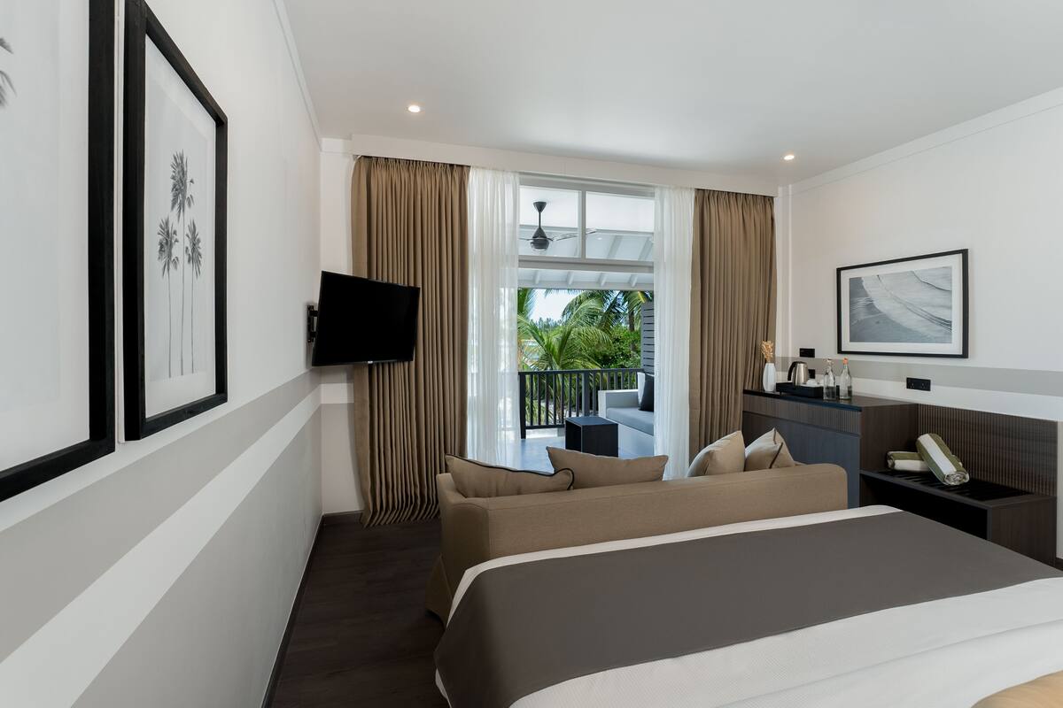 Habitación de hotel con cama, televisor, escritorio y balcón con cortinas.