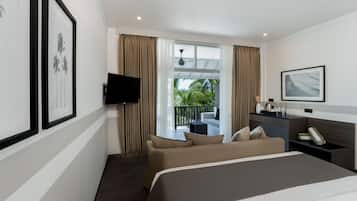 Habitación de hotel con cama, televisor, escritorio y balcón con cortinas.