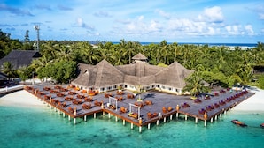 An overwater bungalows with thatched roofs, wooden deck seating, and a view of the ocean. - Sun Siyam Olhuveli (Olhuveli)