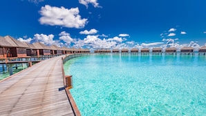 Des bungalows sur pilotis avec une terrasse en bois donnant sur une piscine à l’eau cristalline.