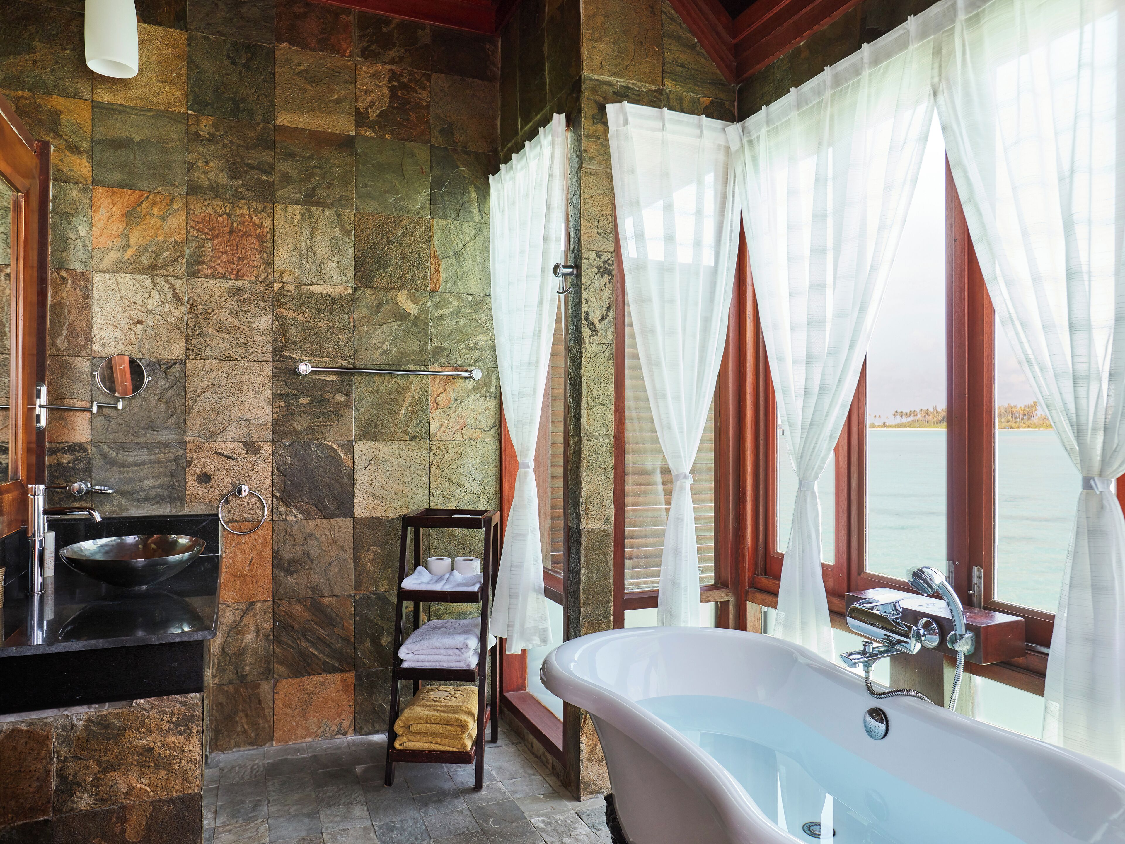 Une salle de bain avec un mur en pierre, une baignoire, un lavabo et une fenêtre avec des rideaux.