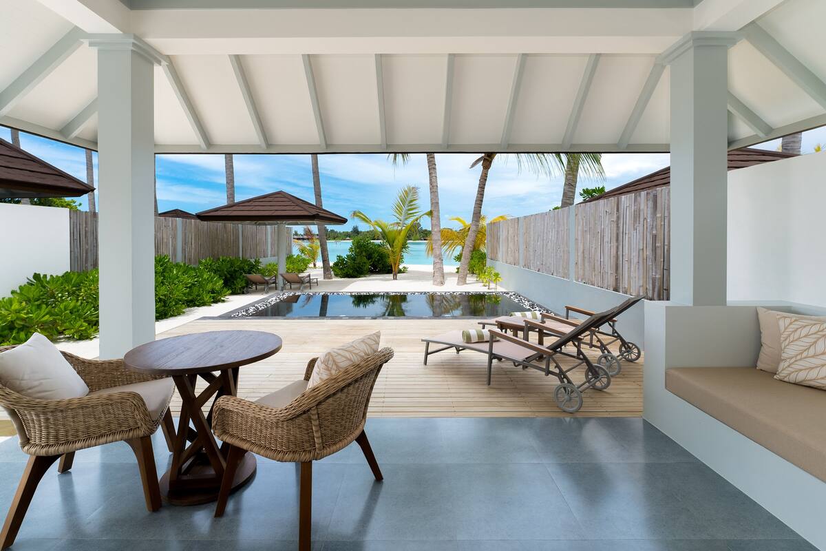 Un espacio al aire libre cubierto con piscina, sillones de descanso y una mesa de comedor.