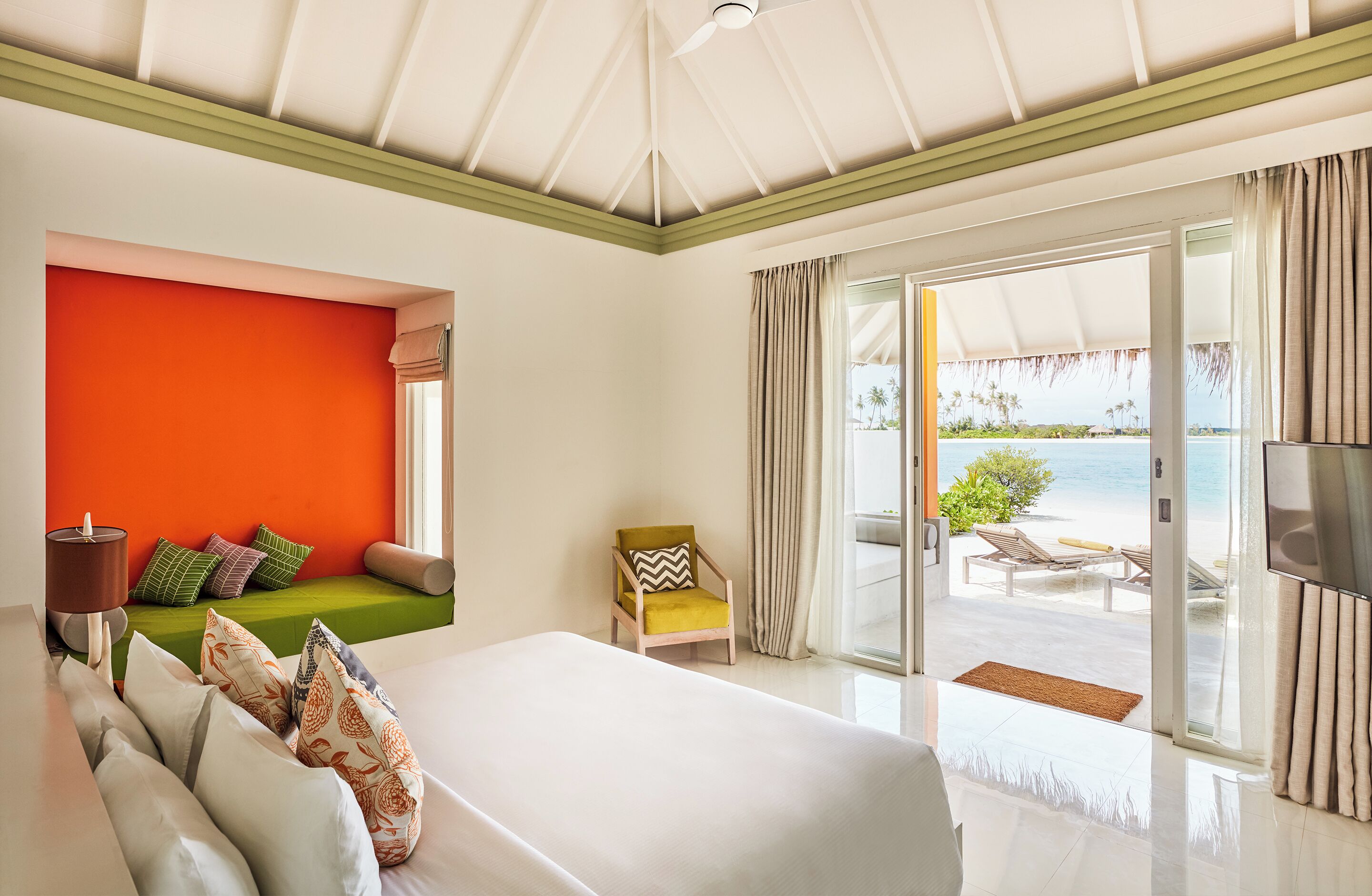 A hotel room with a bed, a green sofa, a TV, and a view of the beach.