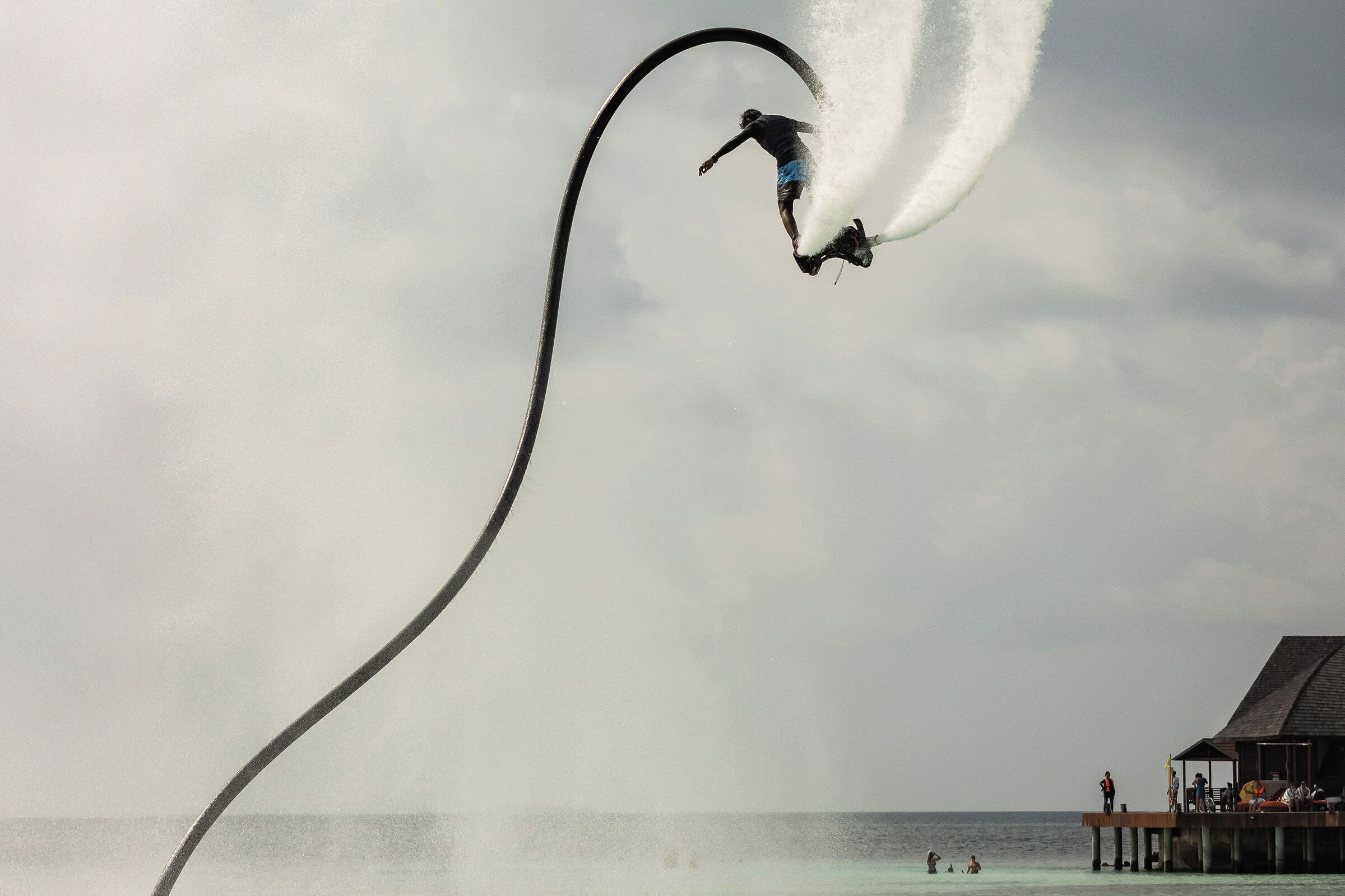 Una persona realizando una acrobacia con un chorro de agua sobre una tabla de surf, con un largo rastro visible.