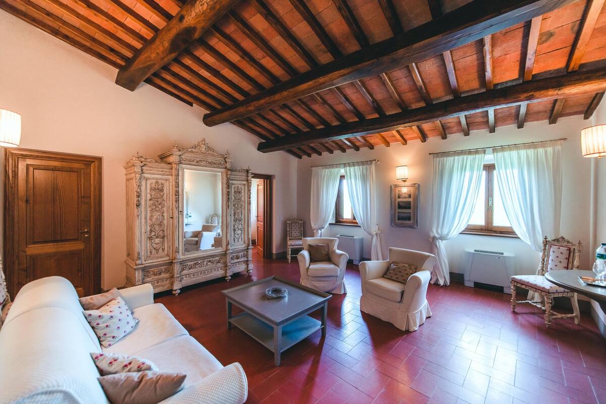 A spacious living room with a high wooden ceiling, a white sofa, a coffee table, and two armchairs.