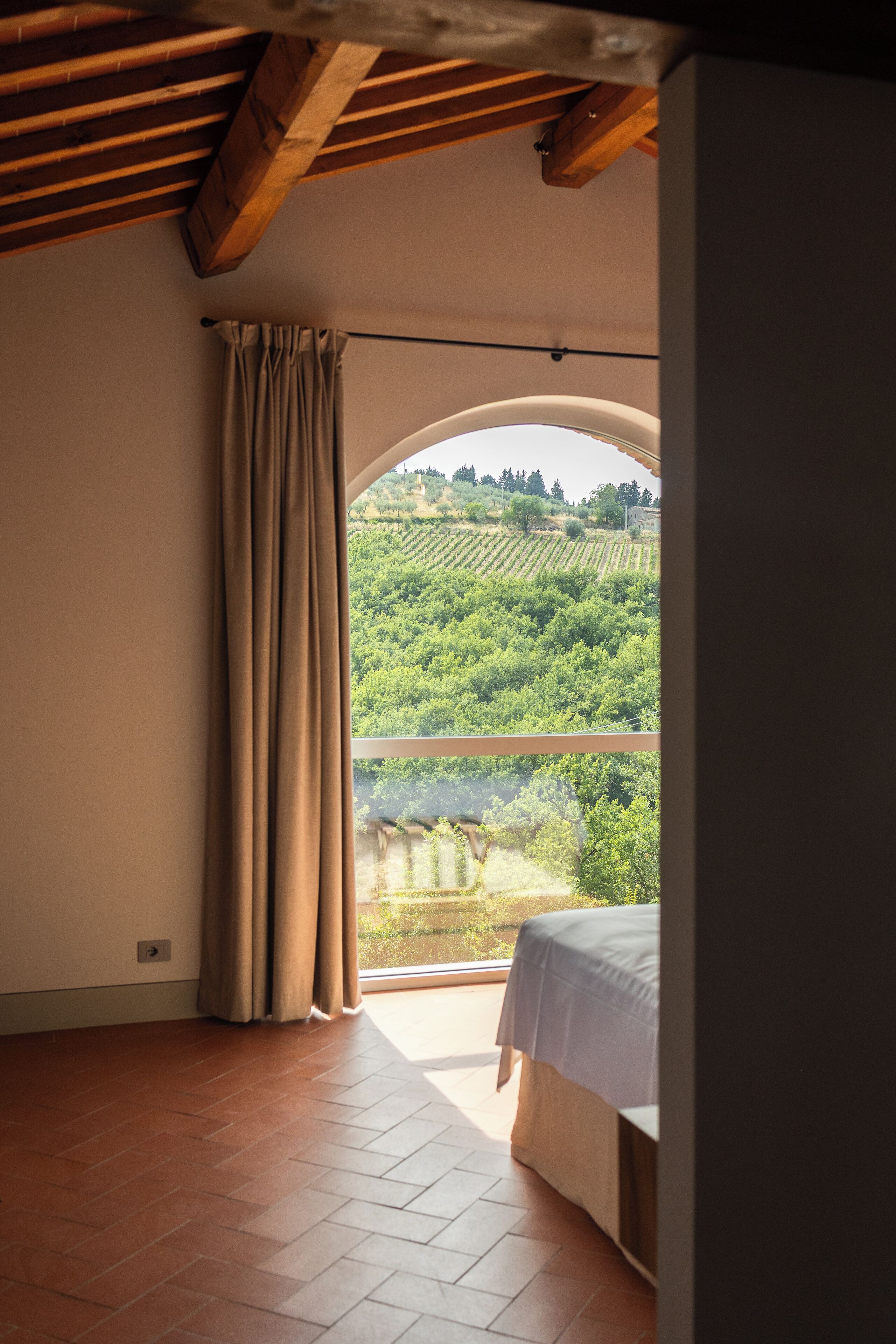 A room with a bed, a window with curtains, and a view of a vineyard.
