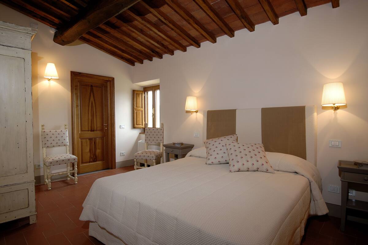A bedroom with a large bed, two bedside tables, a wooden wardrobe, and two chairs.
