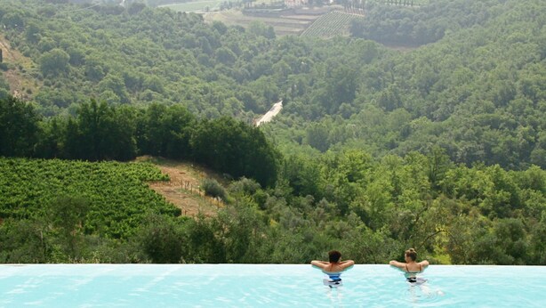 A pool with a view of a lush valley and distant buildings. - Castello Vicchiomaggio (Greve in Chianti)