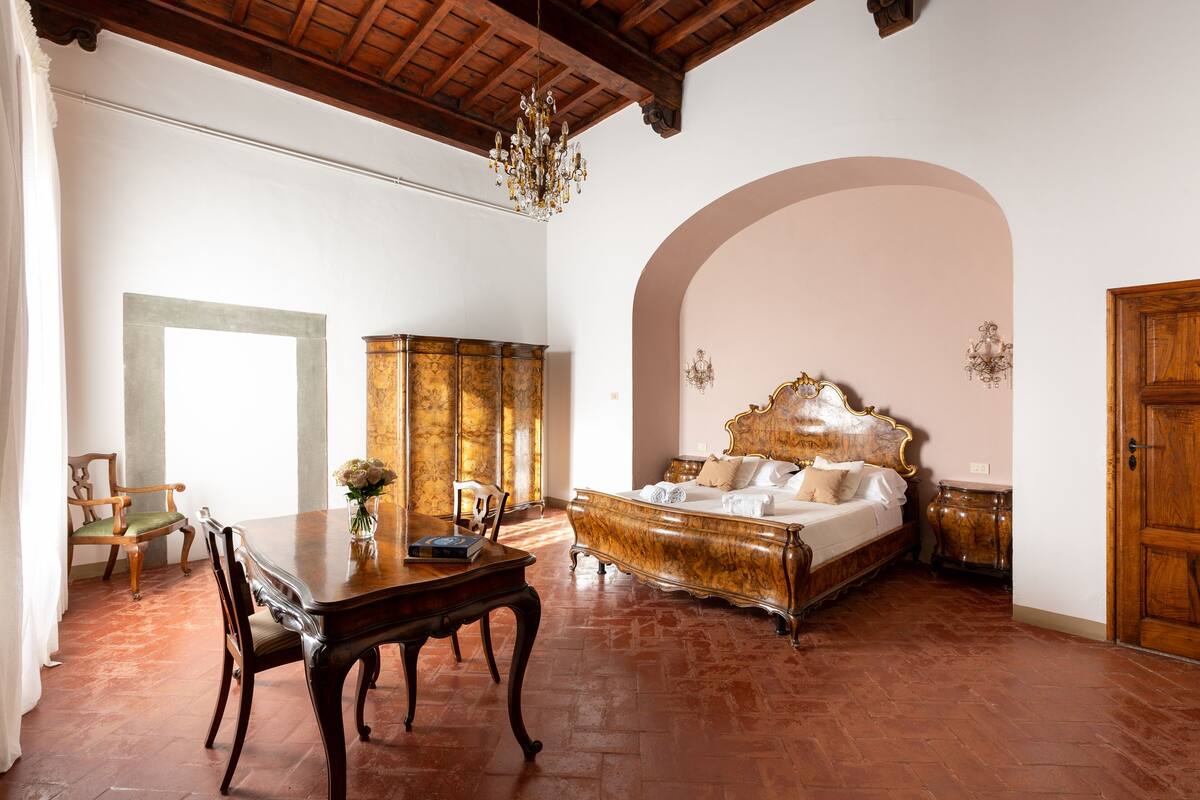 A spacious room with a large bed, a dining table with chairs, and a chandelier.