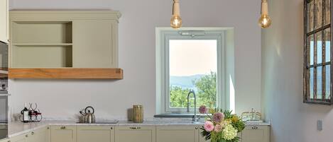 A kitchen with a wooden table, a window with a view, and pendant lights.
