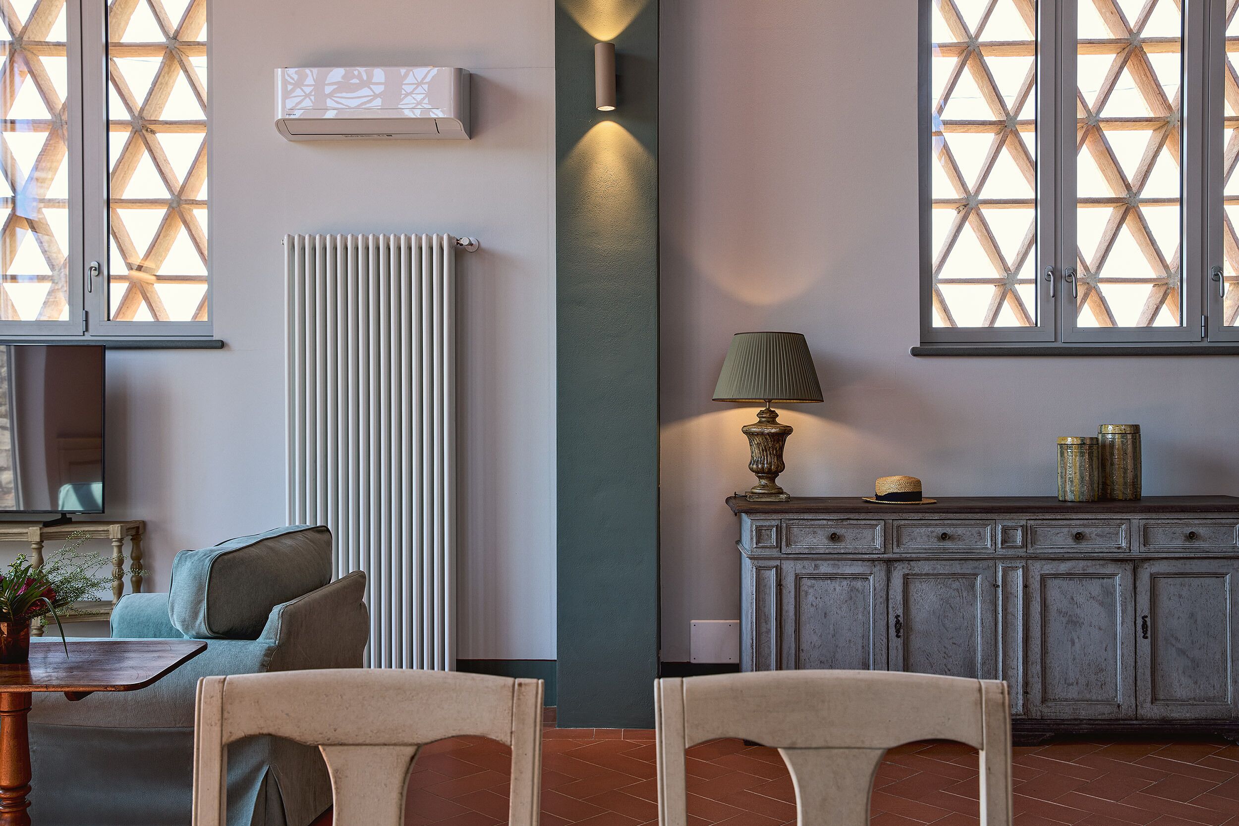 A living room with a sofa, two chairs, a table with a plant, a lamp, a cabinet, and a radiator.