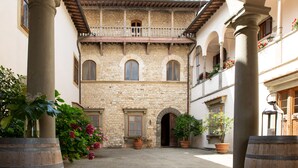 A courtyard with stone buildings, arched doorways, and potted plants. - Castello Vicchiomaggio (Greve in Chianti)