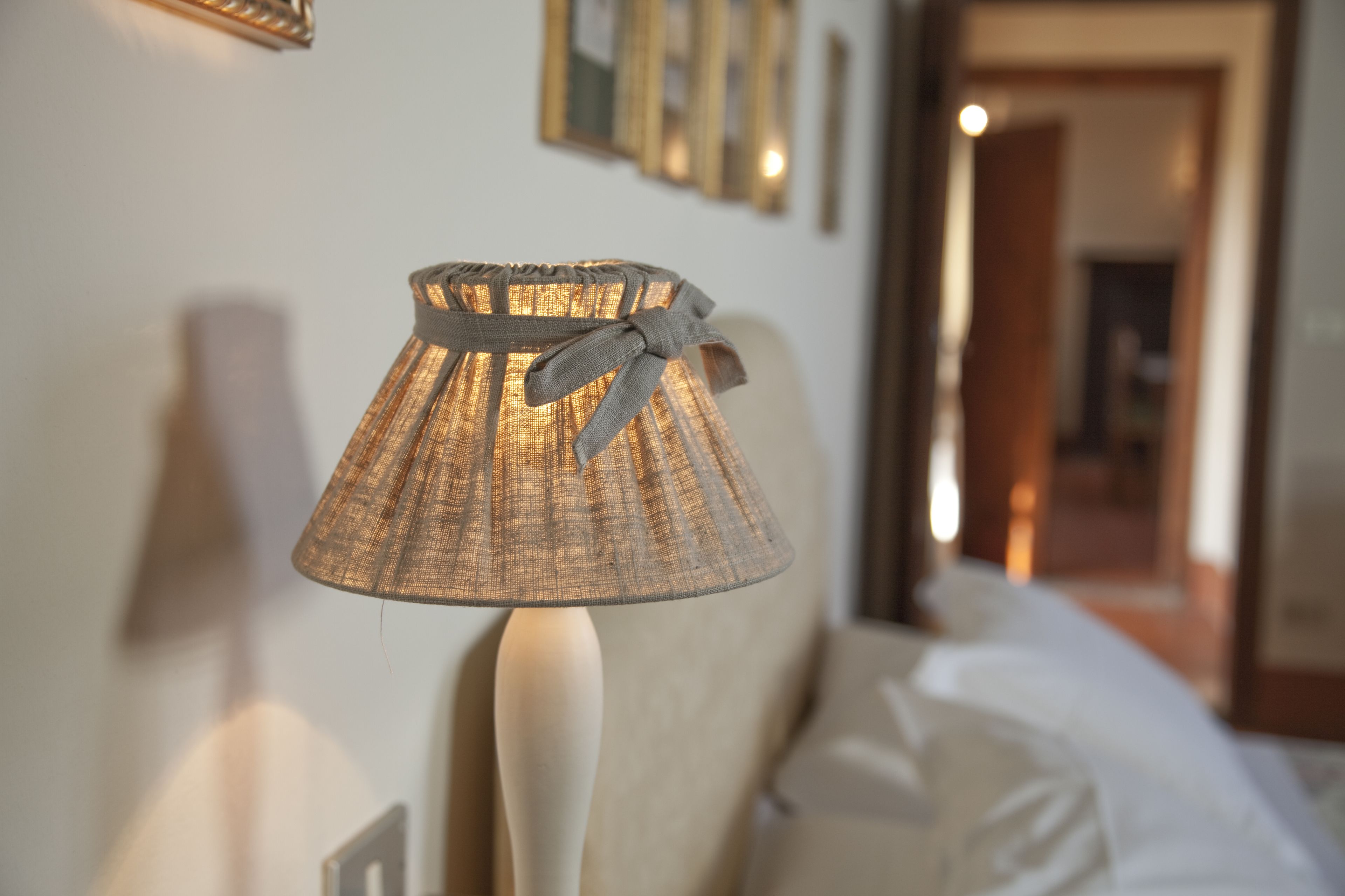 A lamp with a woven shade and a ribbon on a bedside table in a hotel room.