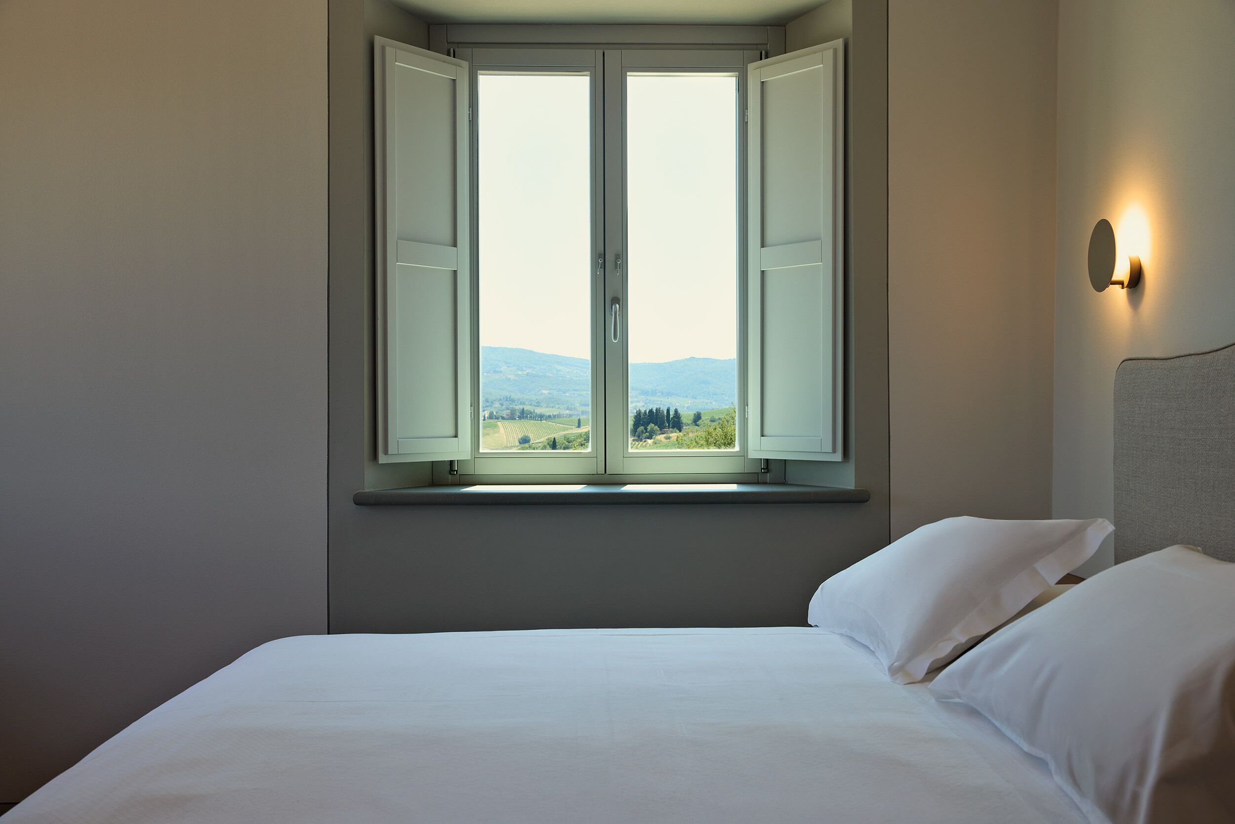 A bedroom with a large window, a bed, and a wall-mounted light.