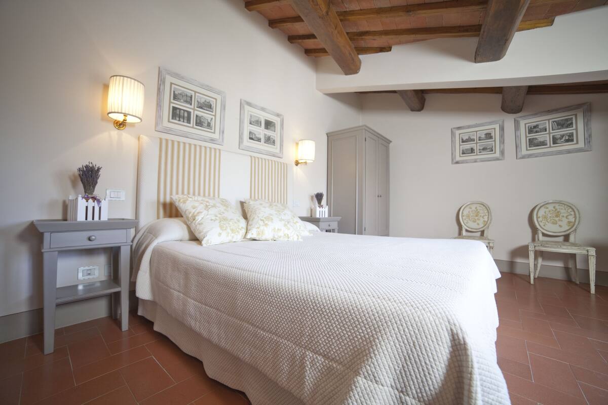 A bedroom with a large bed, two bedside tables, a wardrobe, and wall-mounted picture frames.