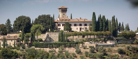 A historic building with a tower, surrounded by trees and a stone wall.