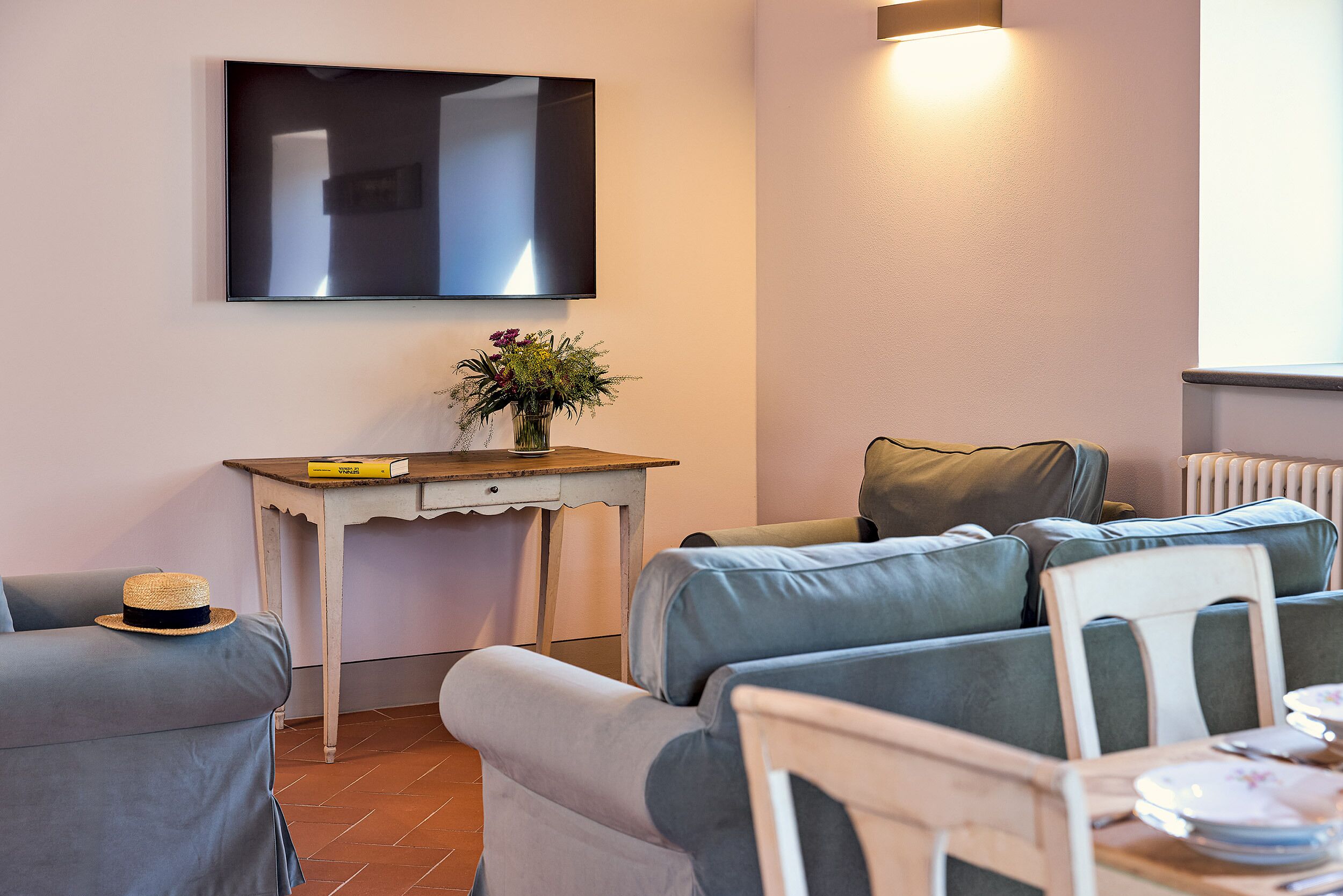 A living room with a sofa, a small table with a vase of flowers, and a flat-screen TV mounted on the wall.