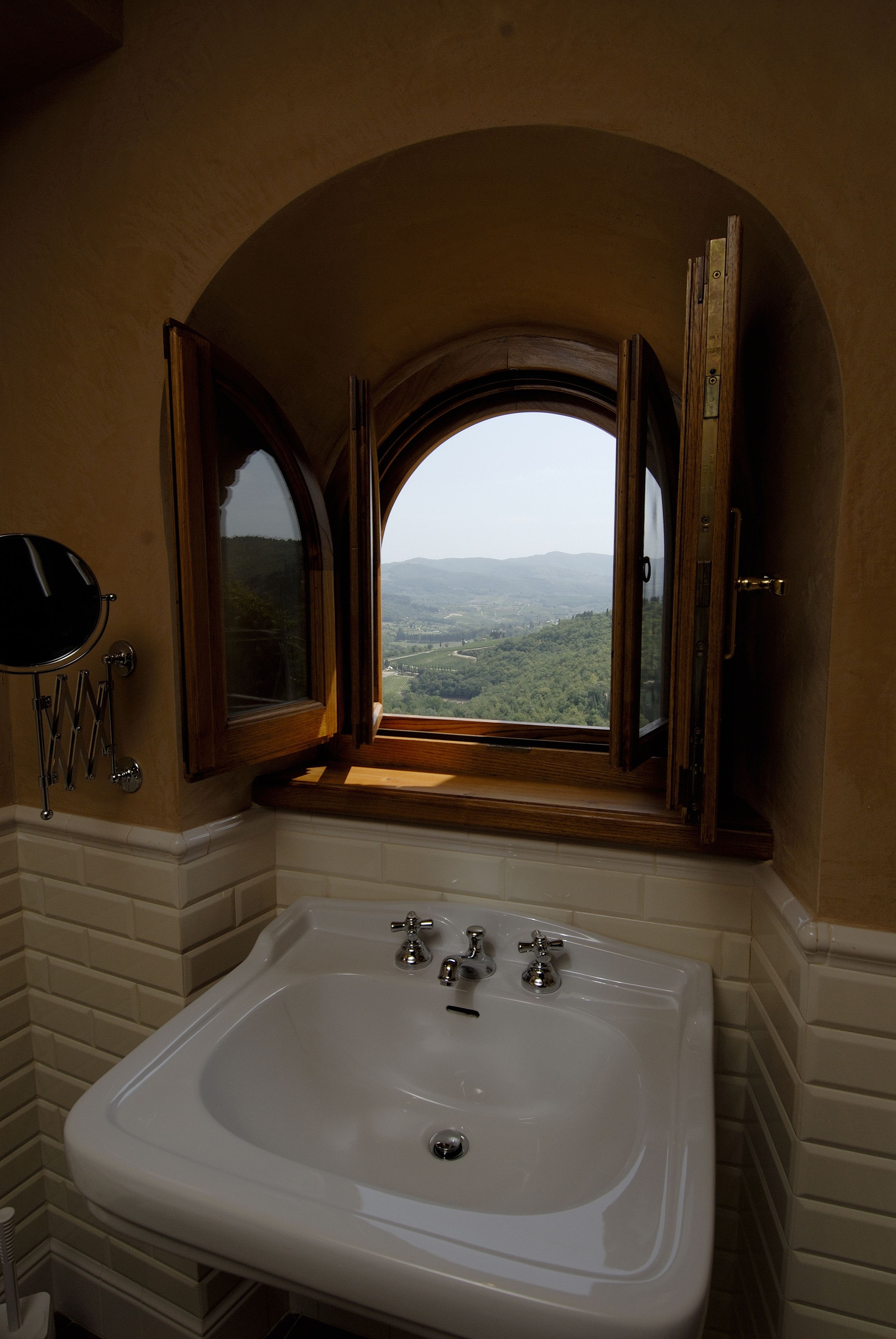 Un baño con un lavamanos grande de color blanco, un espejo y una ventana con la puerta abierta.