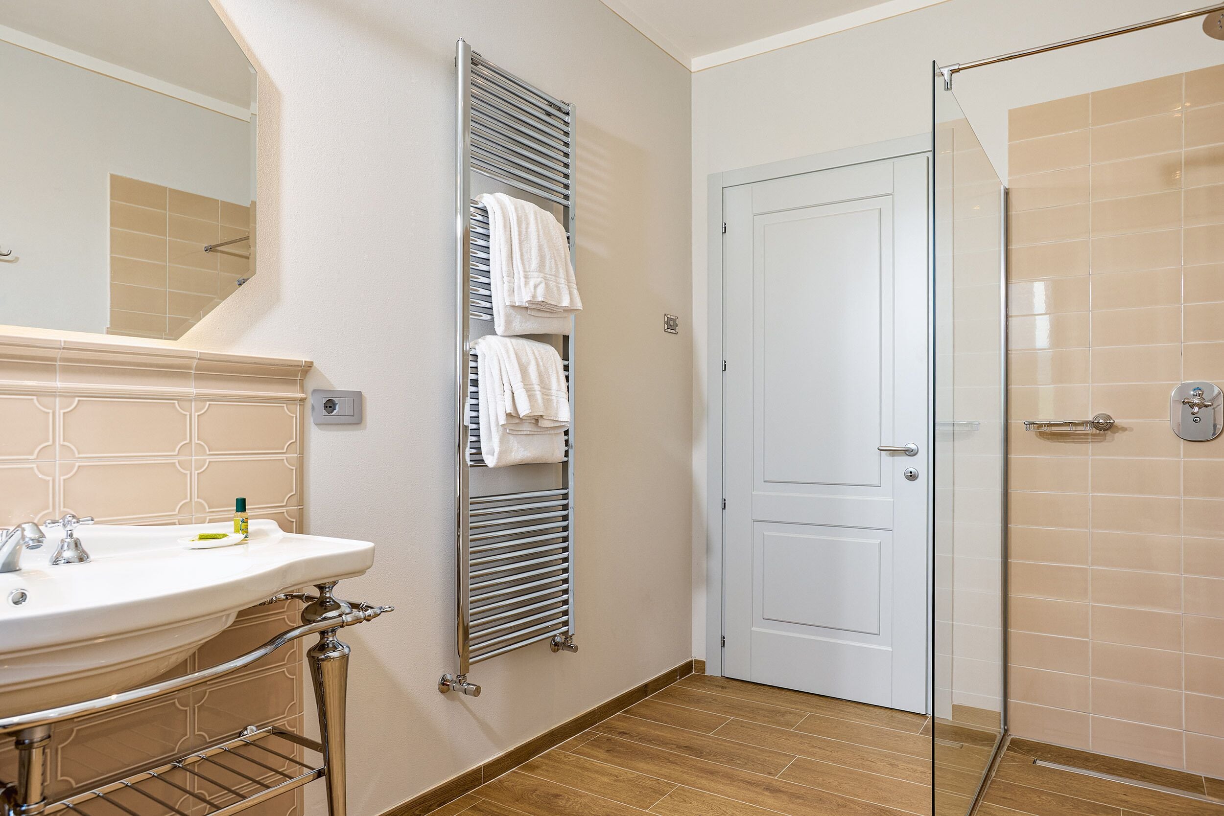 A bathroom with a sink, mirror, towel rack, and a door leading to a shower area.