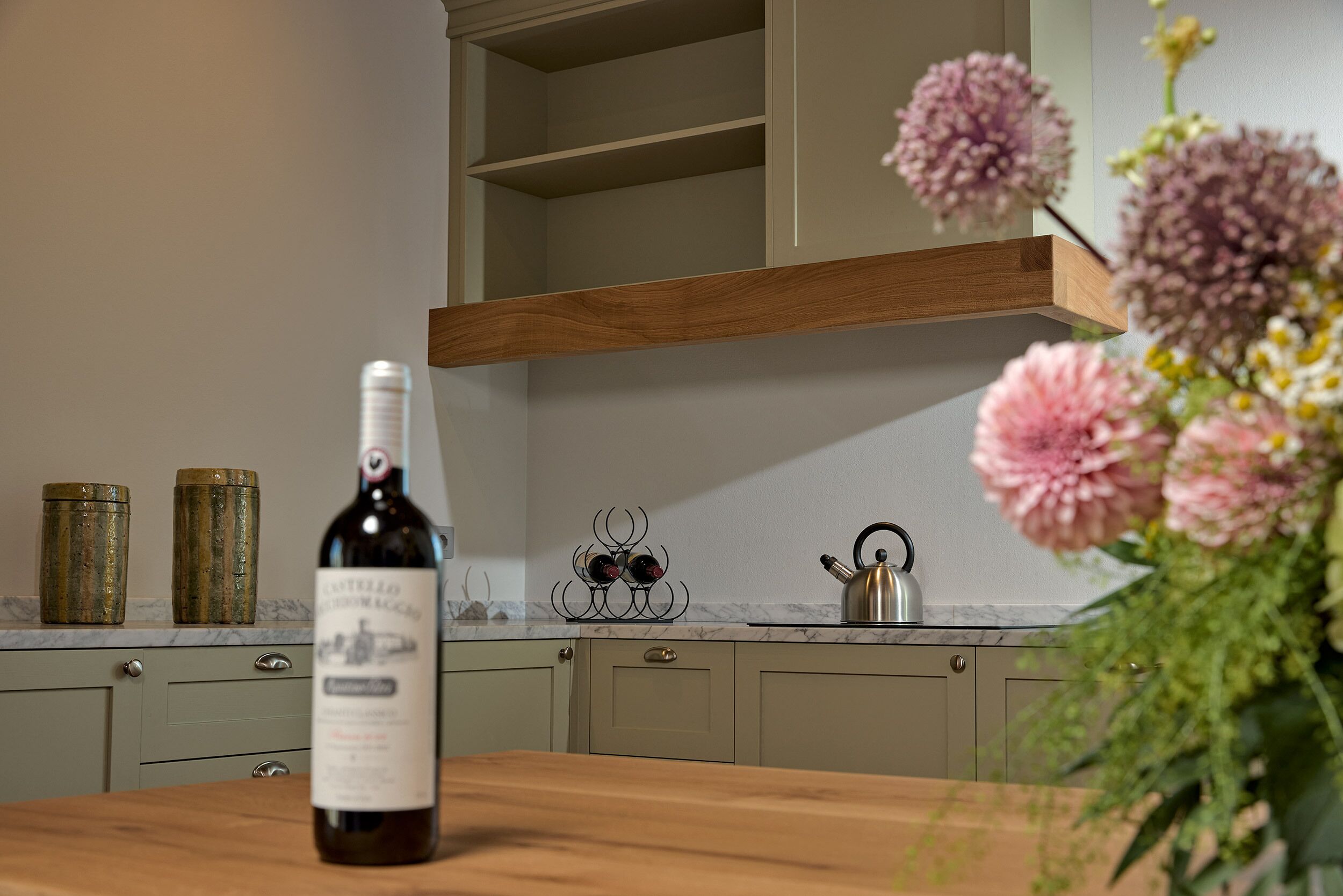Uma cozinha com uma mesa de madeira, uma garrafa de vinho e um vaso de flores.