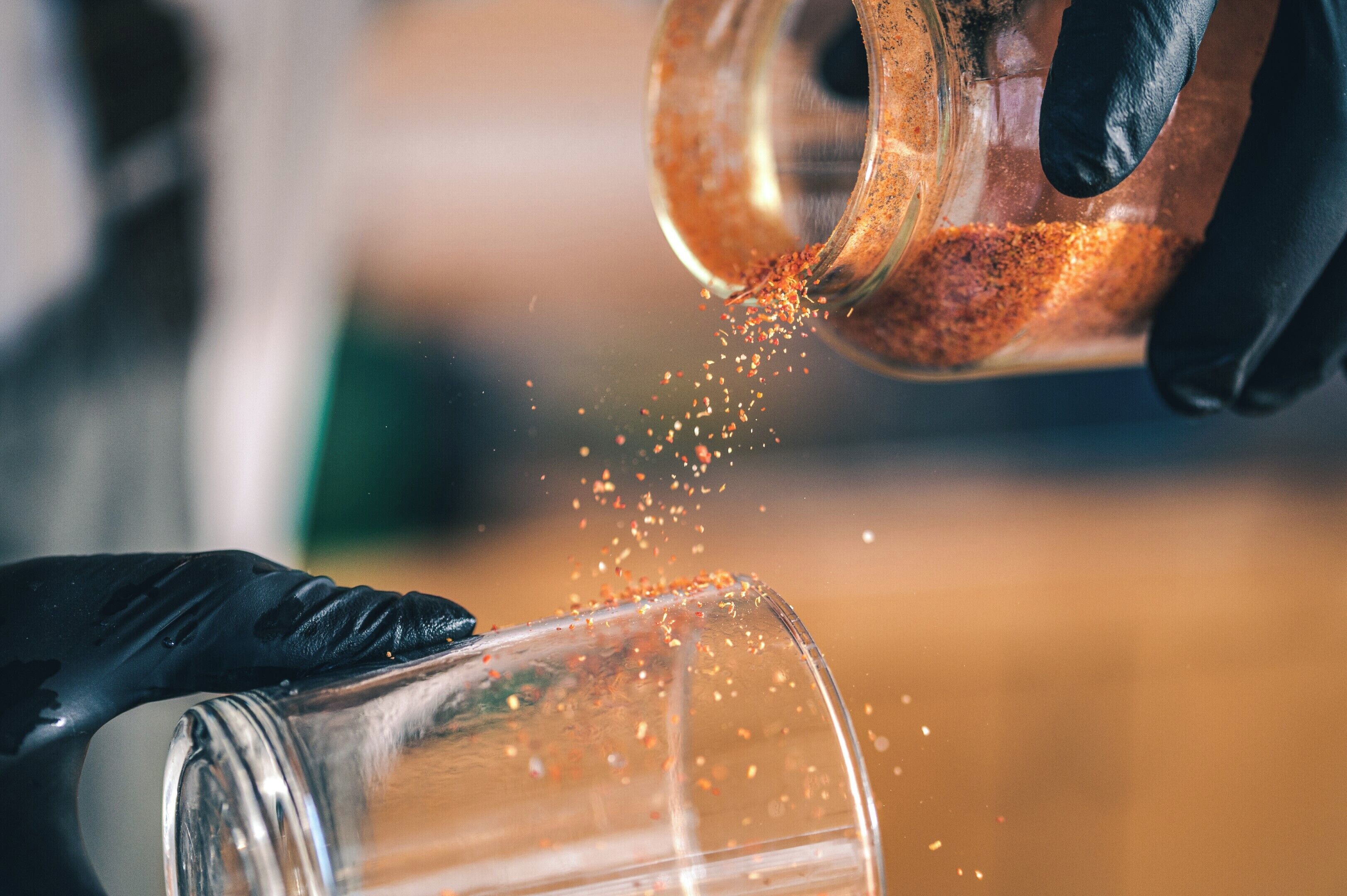 A person wearing black gloves pouring a granular substance into a clear container.