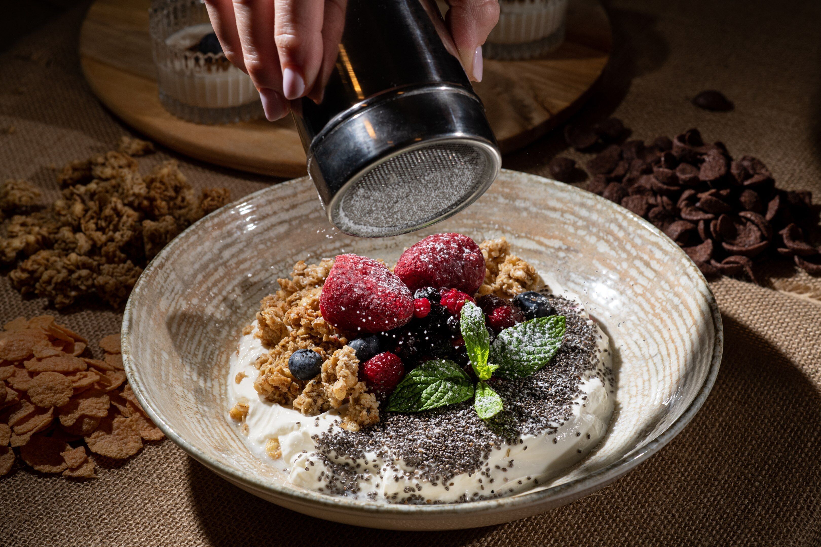 A bowl of cereal with fruits and a powdered substance being sprinkled on top.