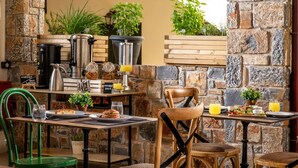 A breakfast setup with a stone wall, a coffee station, and a table with breakfast items. - Villa Elite by Checkin (Hersonissos)